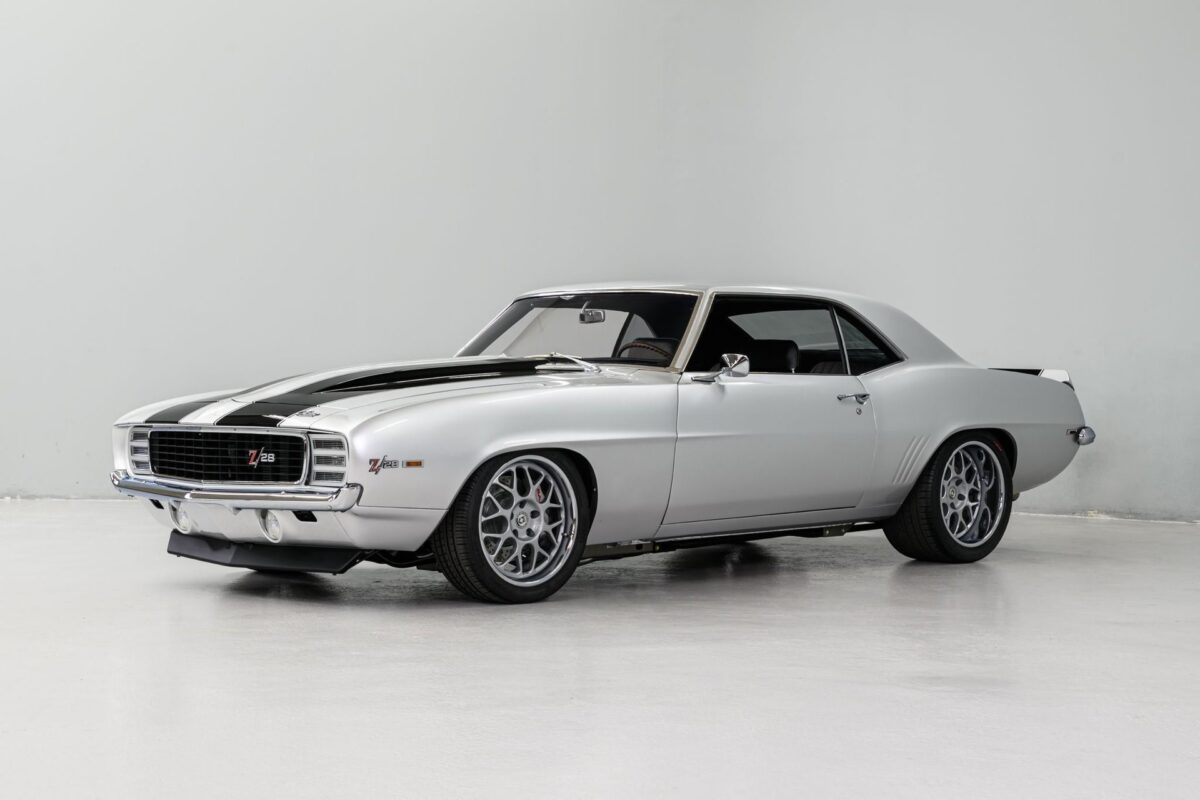 A white 1969 chevrolet camaro ls3 with a black stripe is parked in a white garage.
