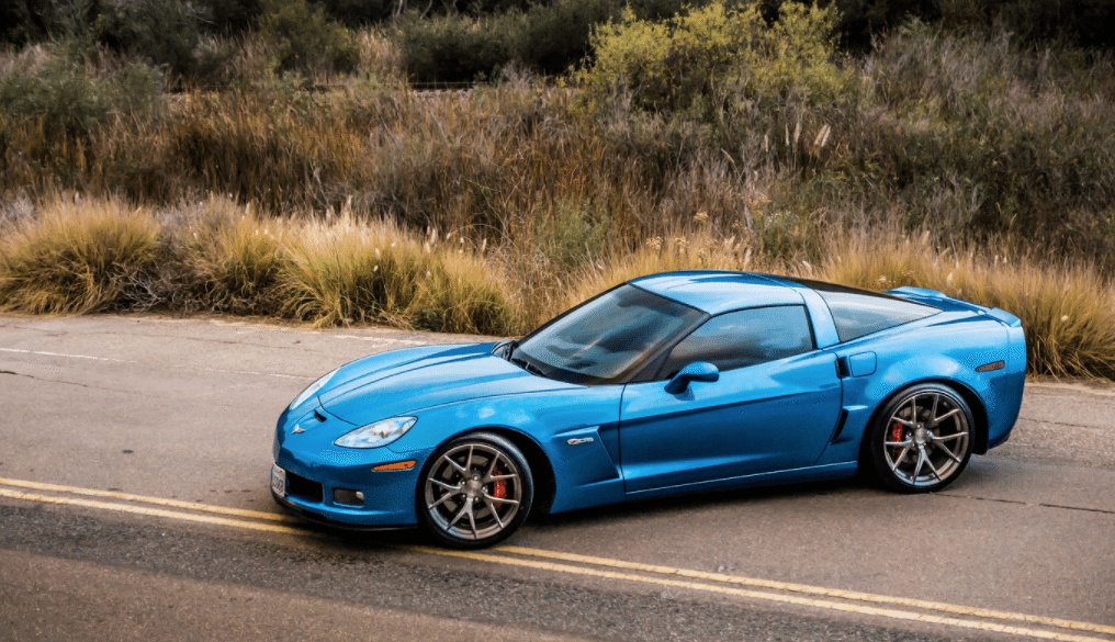 Blue Devil Corvette about to make a 3 point turn on a country road. Tall grass is growing along the shoulder of the road.