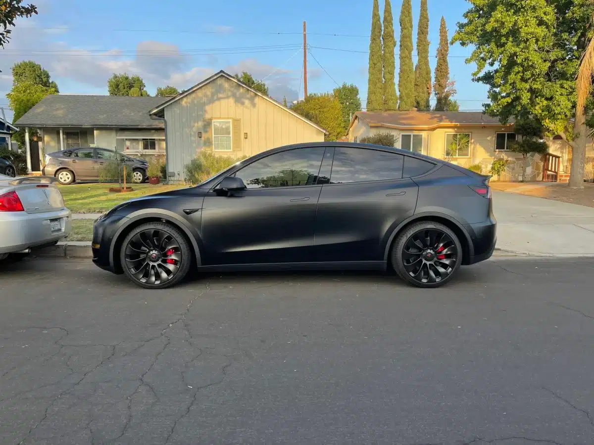 A black matte tesla model y parked on the street in front of a house.