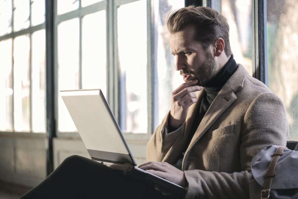 A man is sitting in front of a window with a laptop on his lap.