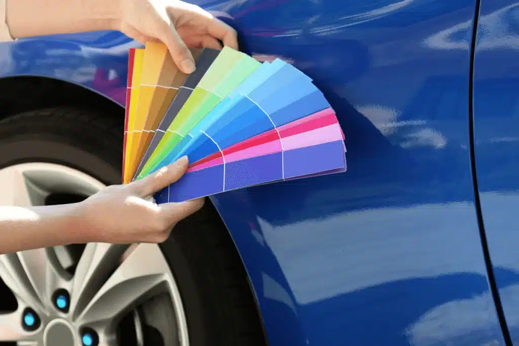 Someone holding colour swatches next to a blue Corvette.