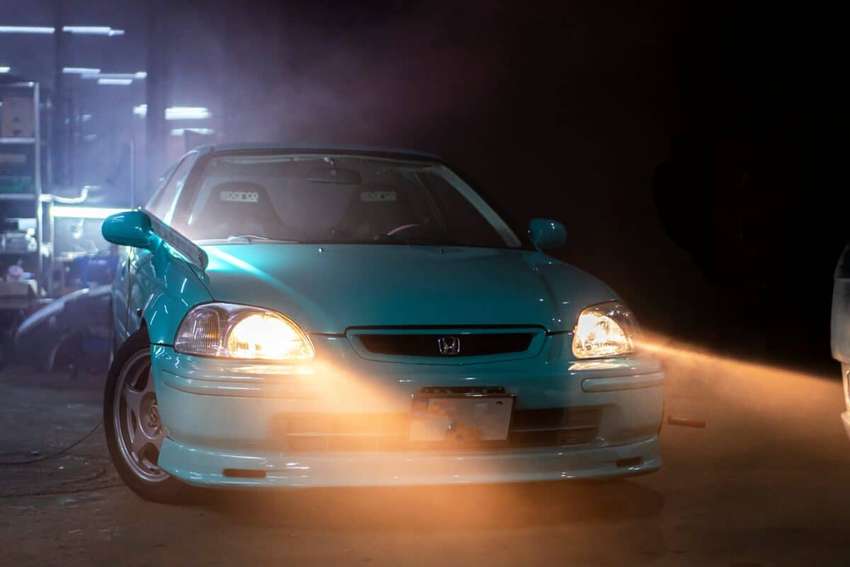 A light blue Honda Civic in the night has its headlights shining.