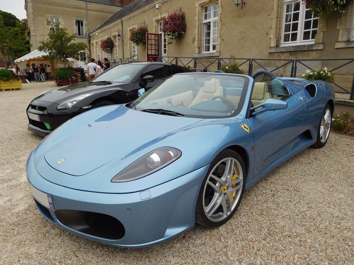 another light blue ferrari is parked outside a historical home in england. light blue ferraris are considered trendy for young posh people.