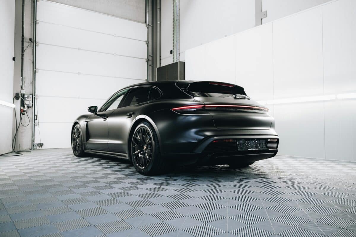 A black car with stealth PPF in a bright garage with lots of sunlight, white walls, and cement tile flooring.