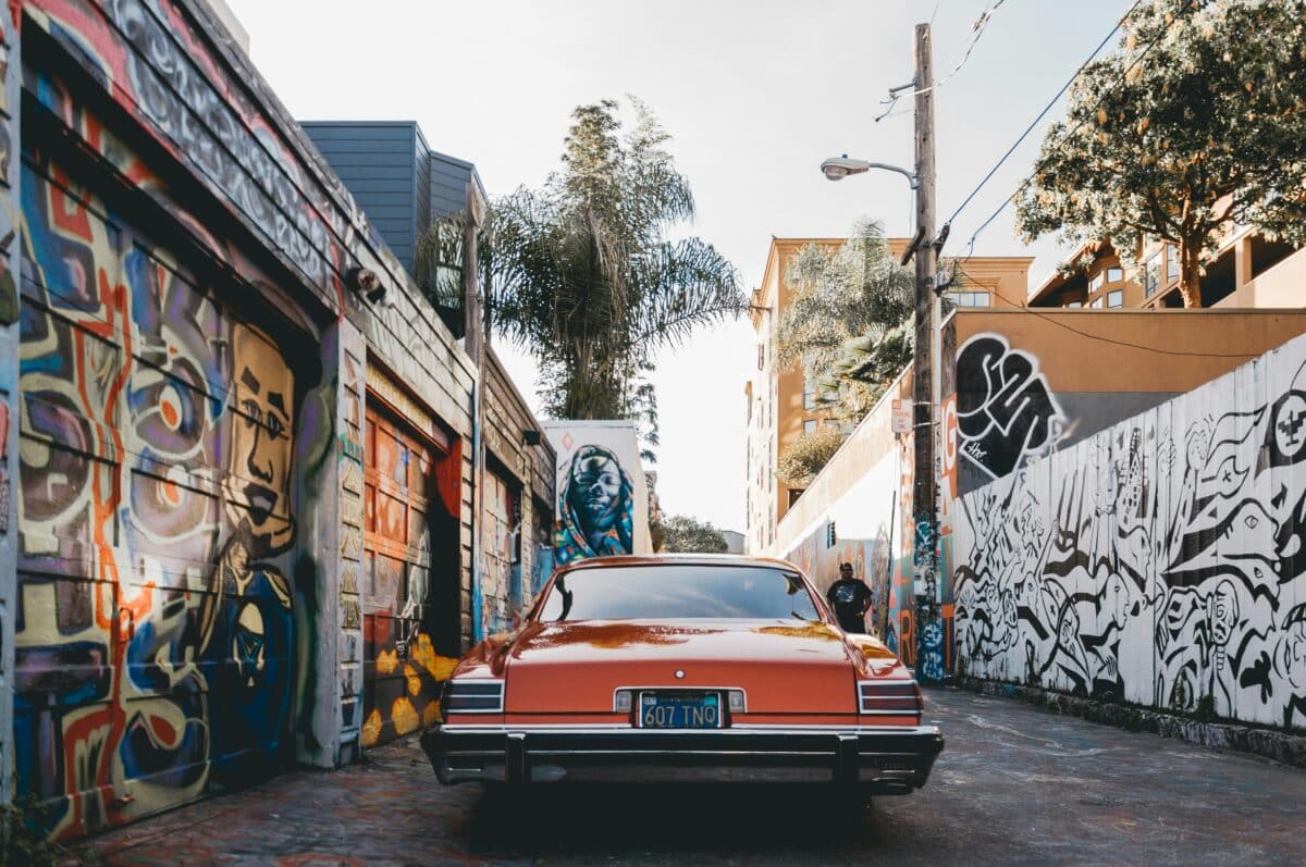 A muscle car or vintage car with tinted windows in San Francisco Bay Area, in a graffiti alley. 