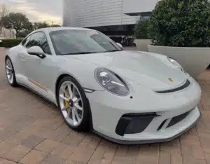 A dolphin grey porsche is parked on a brick parking lot on a cloudy day.