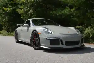 A fashion grey porsche parked on a street beside bushes.