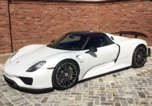 An oryx pearl white Porsche is parked on a brick road in front of a brick building.