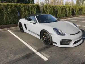 A sports classic grey Porsche parked in a parking lot by a hedge.