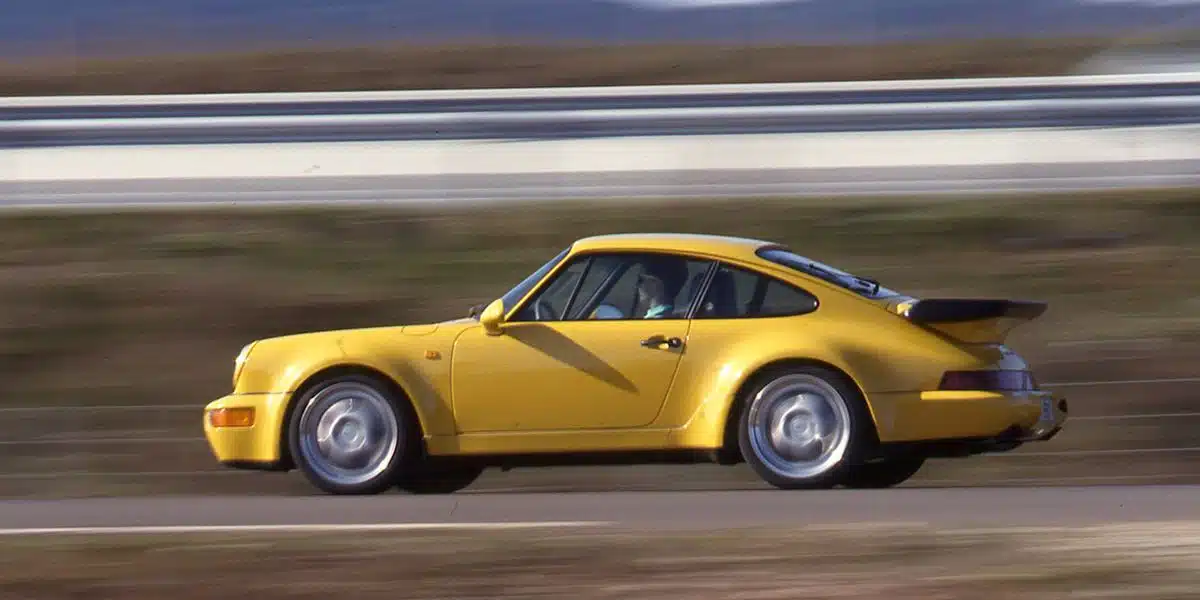 A yellow Porsche whale tail is easy to see as the car is captured in motion on a track,