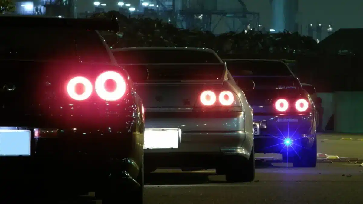 A back view of some Japanese 90's cars driving down a street at night.