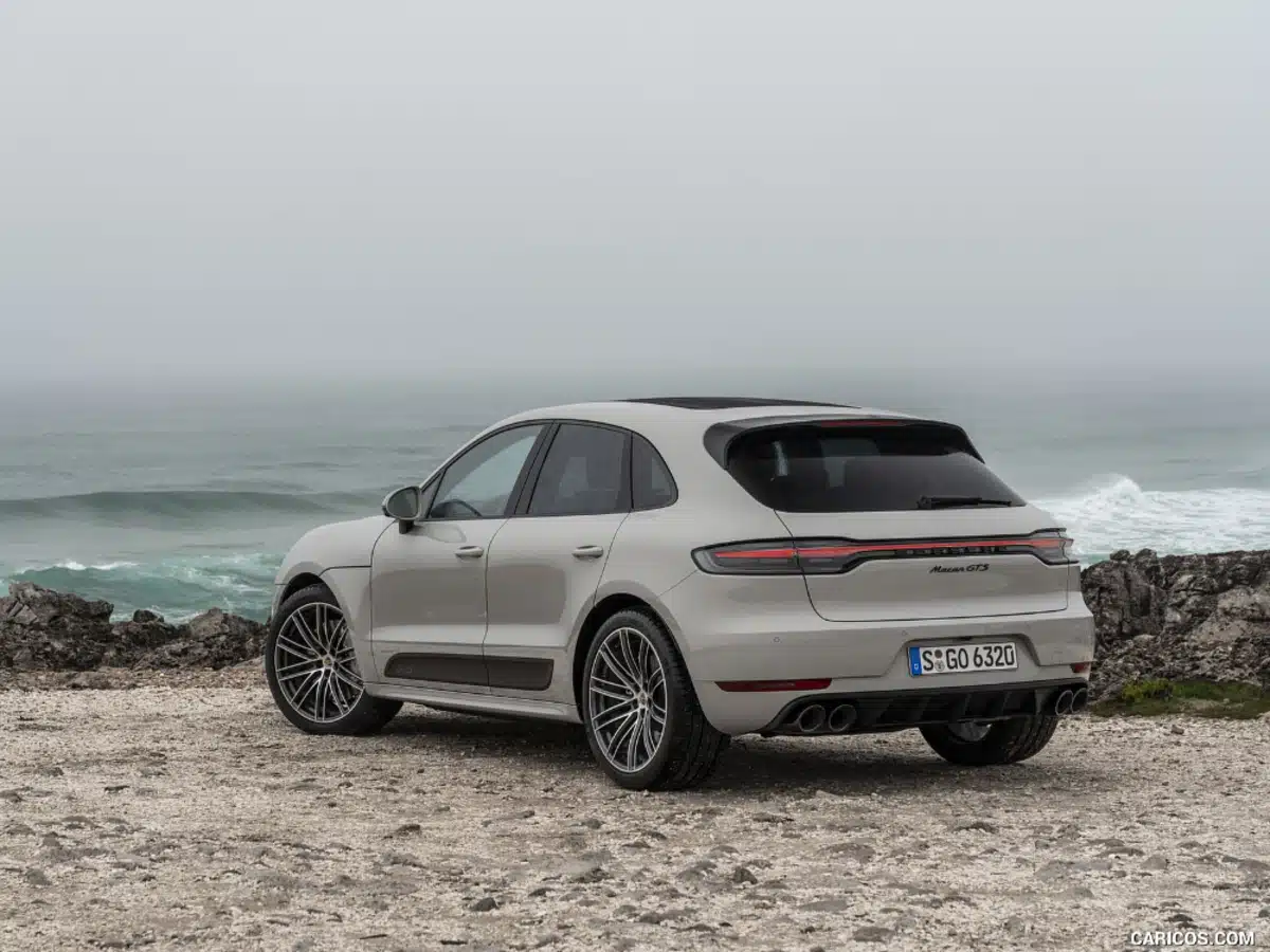 A porsche macan gts in chalk color is parked on a sandy beach on a cloudy day.