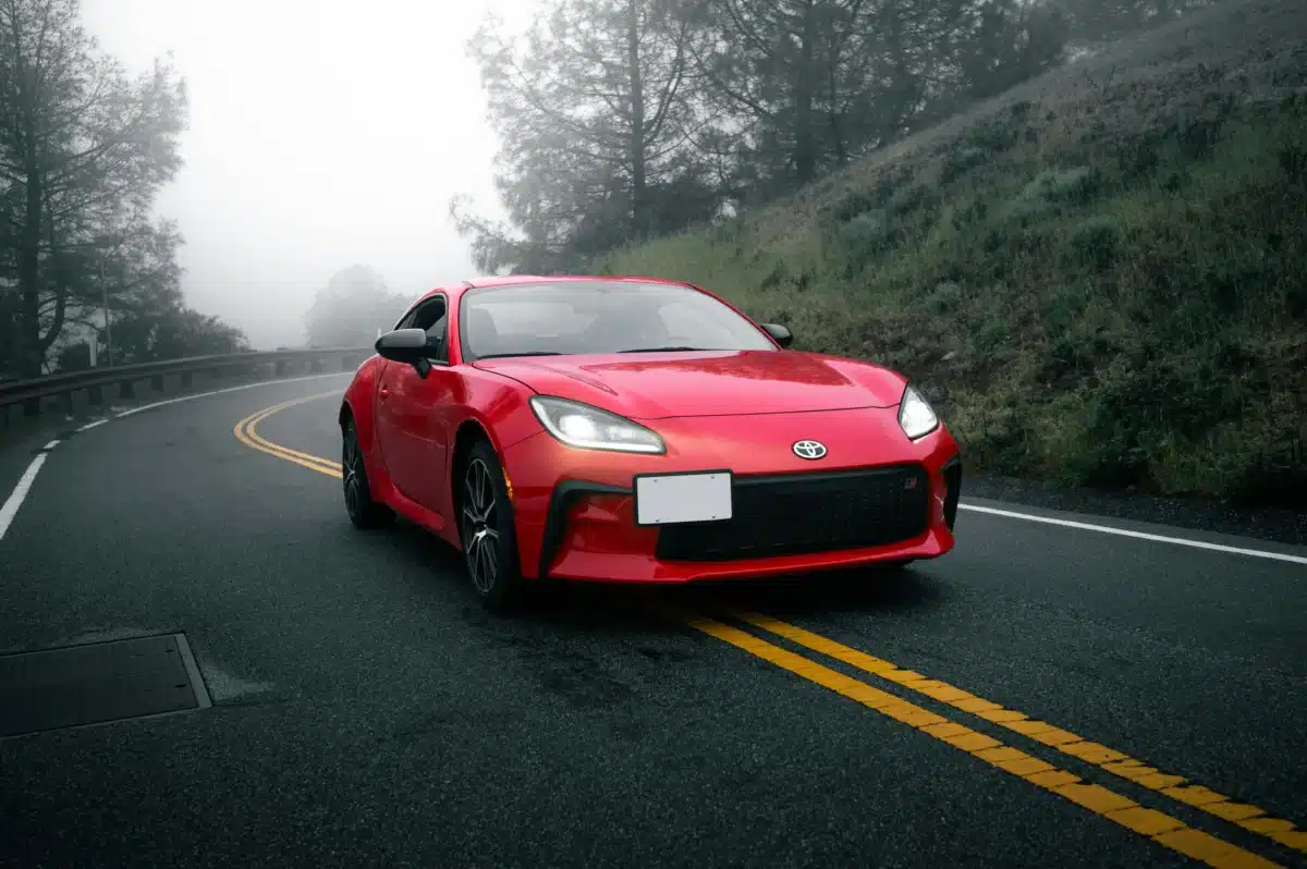 A red Toyota GR86 is driving down a road on a foggy day. The best wheels for GR86 can depend on weather conditions.