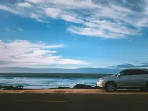 A car is coming into frame from the left as it drives along the coast of California. This is why car detailing California is necessary for car maintenance. 