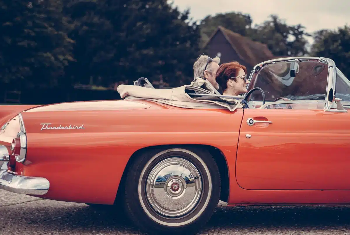 Two people are riding in a red convertible vintage car for film work, probably a historical prooject.