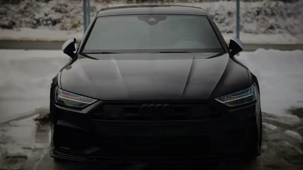 The front end of a black car with chrome delete. The car is parked on a cement road.