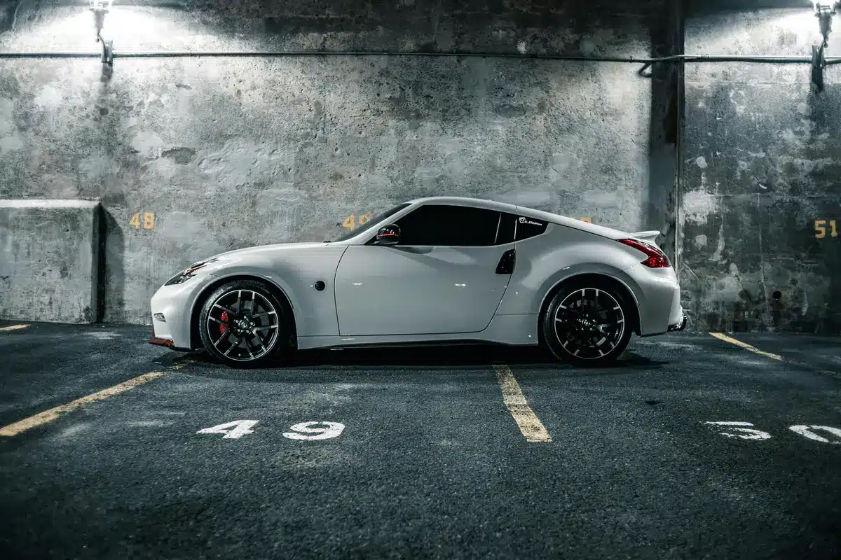 A white sports car is parked in a cement underground parking garage with dark ceramic tinted windows rolled up.