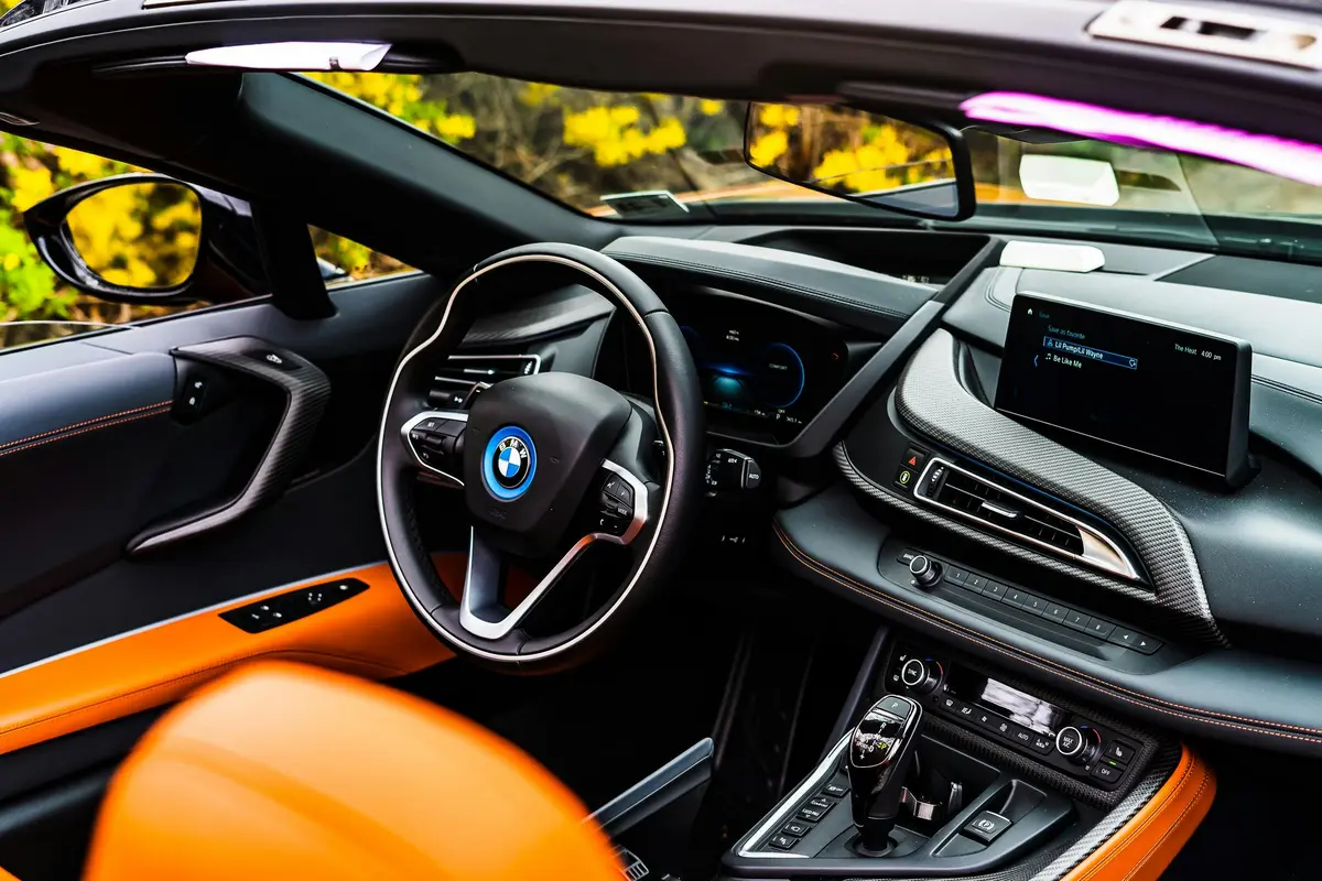 A newly detailed orange and black interior of a luxury BMW near Palo Alto, CA. It's outside, and it's a convertible with the top down. There is some foliage in the background, and it's a sunny day.