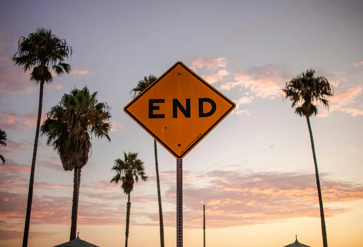 A diamond-shaped yellow road sign is in the center of the photo, which reads 'END'. Palm trees are standing tall in the sky behind it.