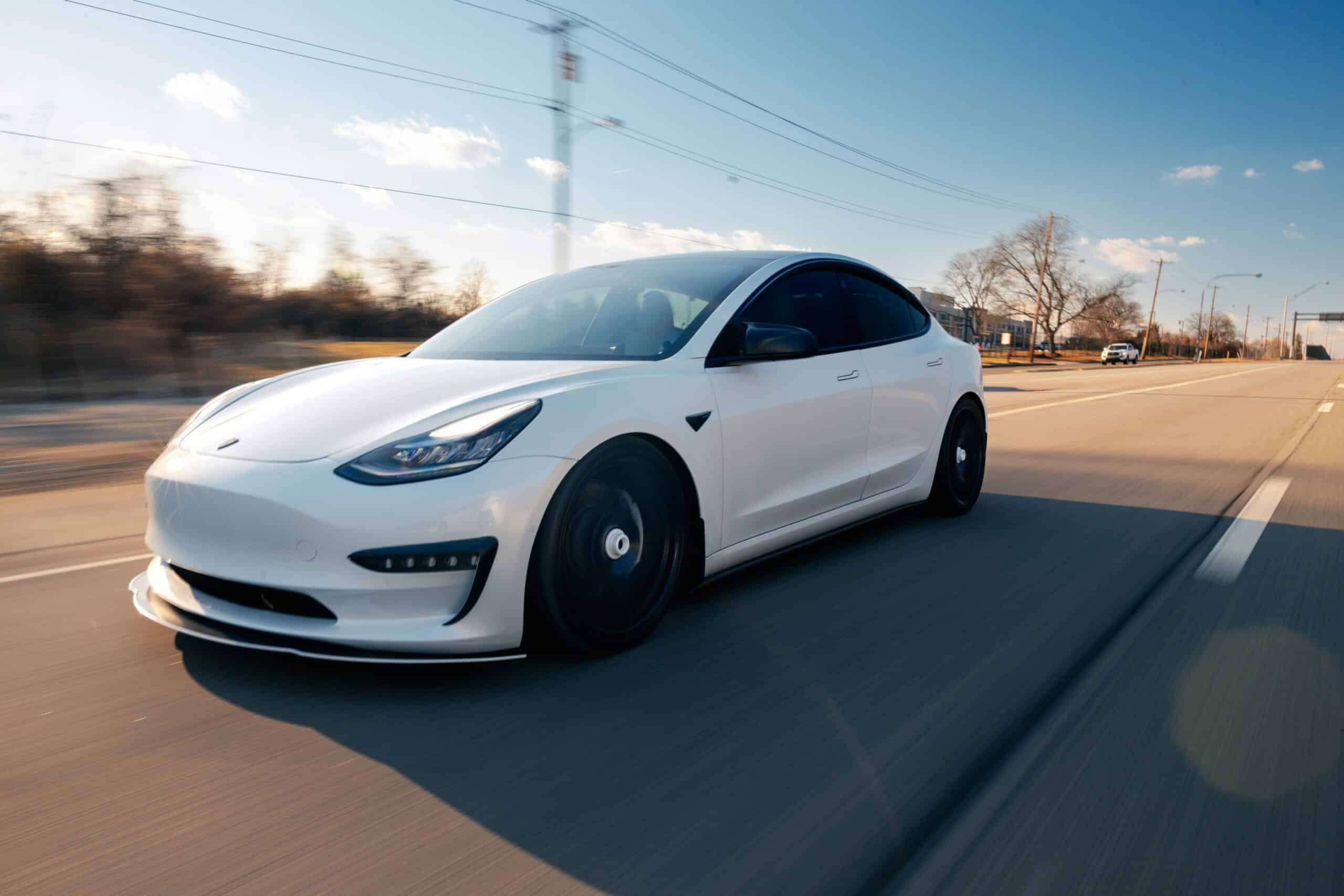 A white Tesla is driving on a road in the sun, needing Tesla paint protection from the UV rays.