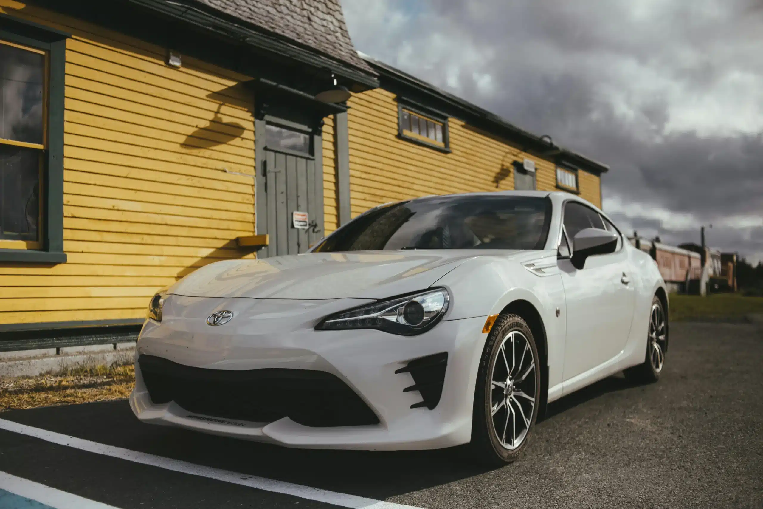 A white car parked in front of a yellow house on a cloudy day.