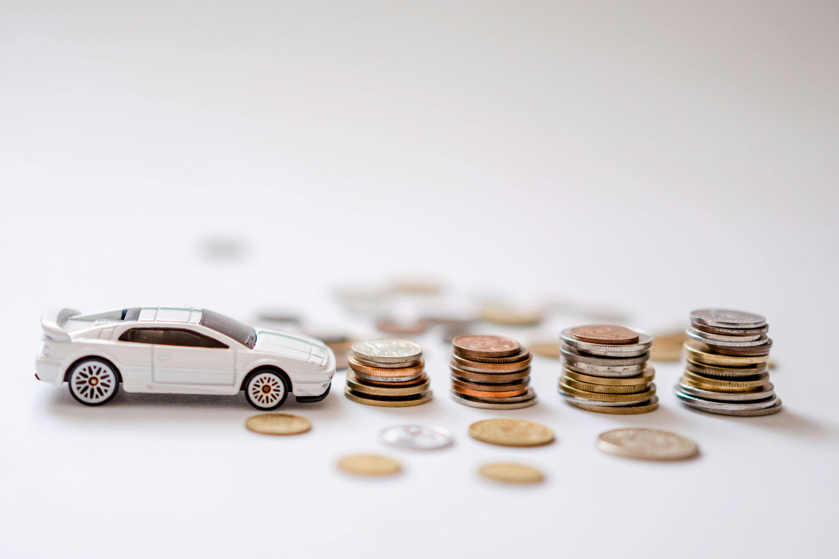 A toy car is facing a row of stacked coins on a white background.