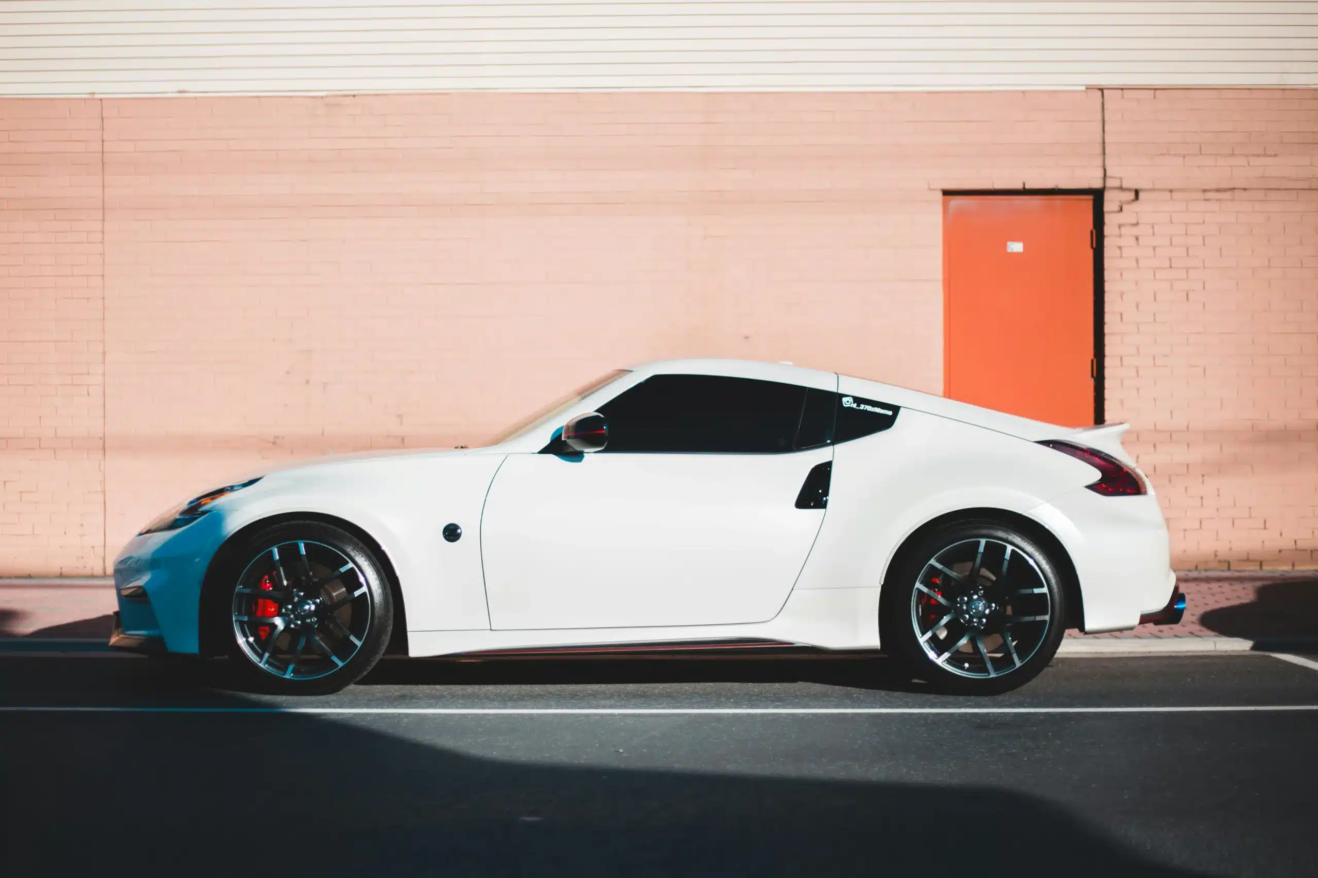 A white sports car with tinted windows in San Leandro parked in front of a pink brick building on a paved lot.