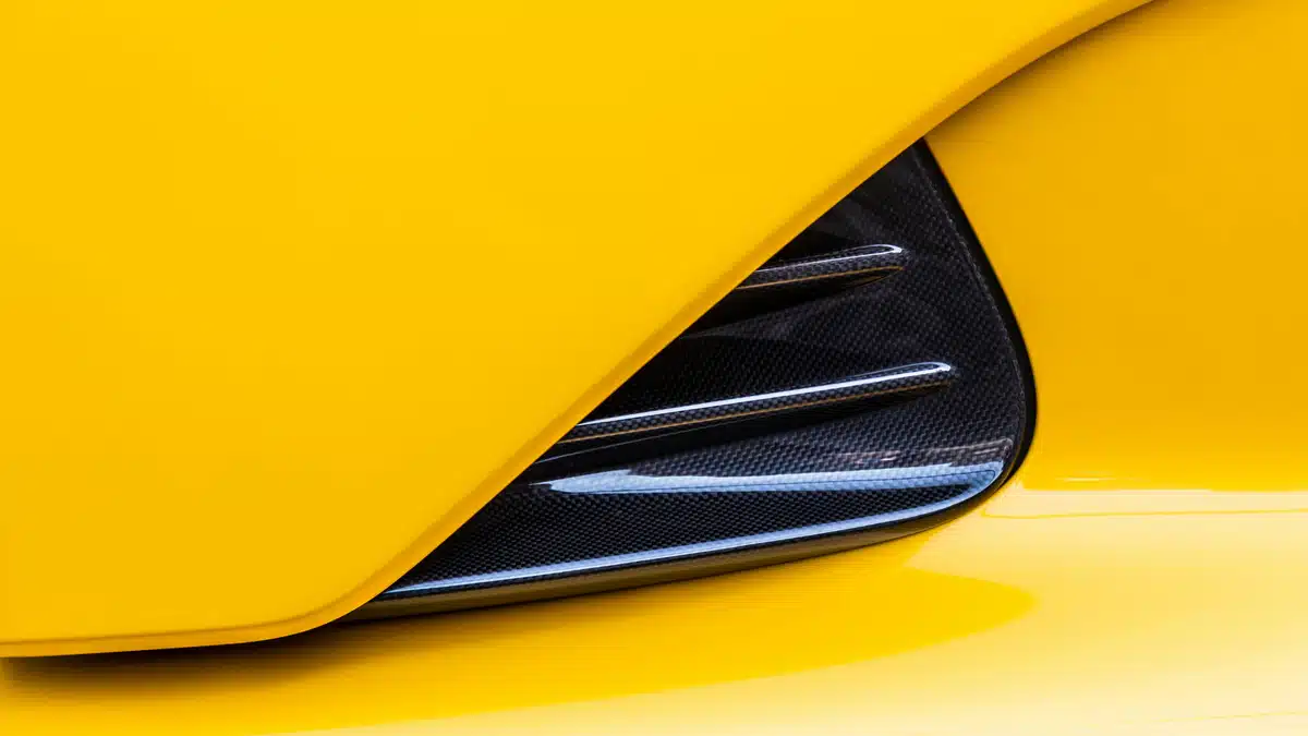 A close-up of a headlight on a Porsche 911 with paint protection film installed over yellow exterior paint.