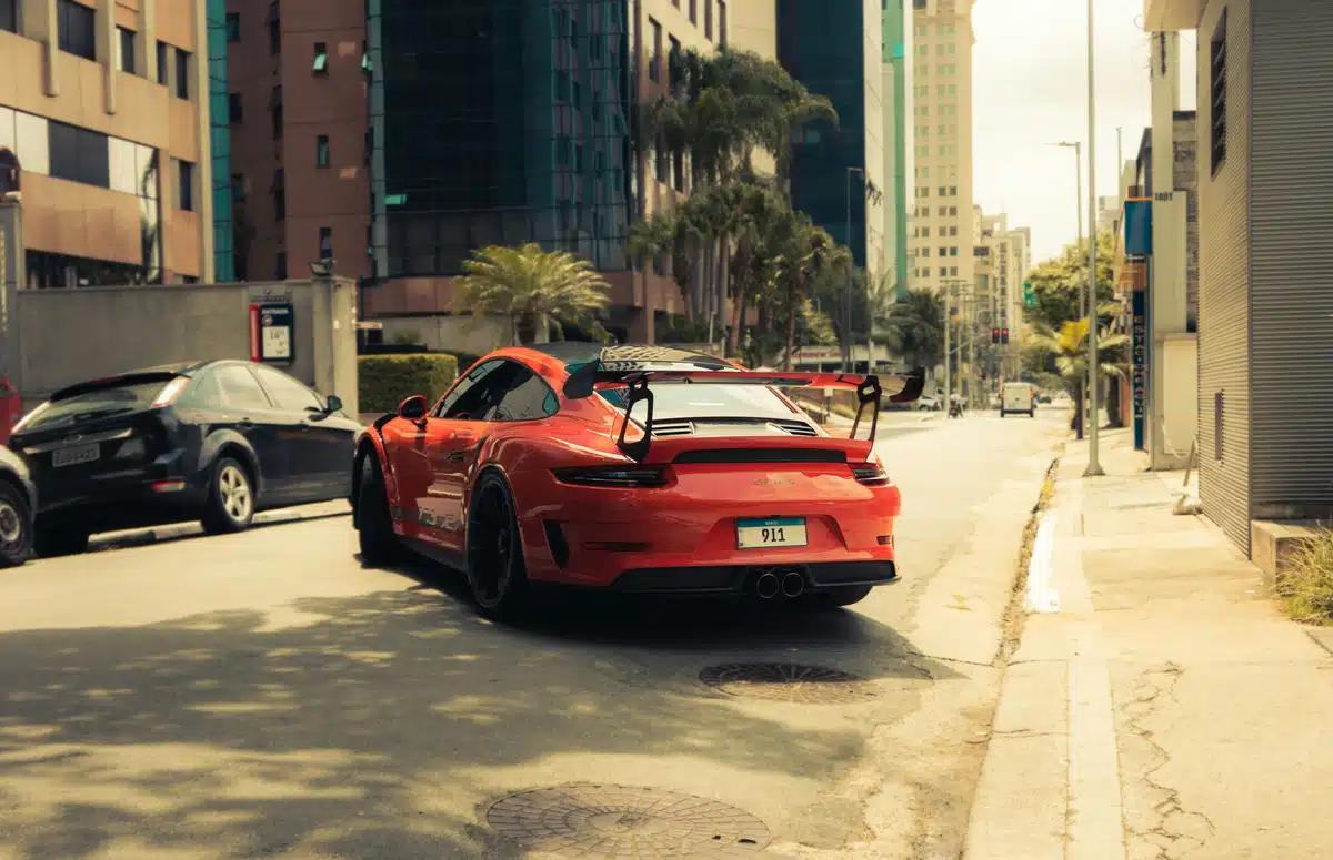 A red paint protected Porsche 911 on a sunny street with palm trees in the background. It's a city area with high rise buildings.