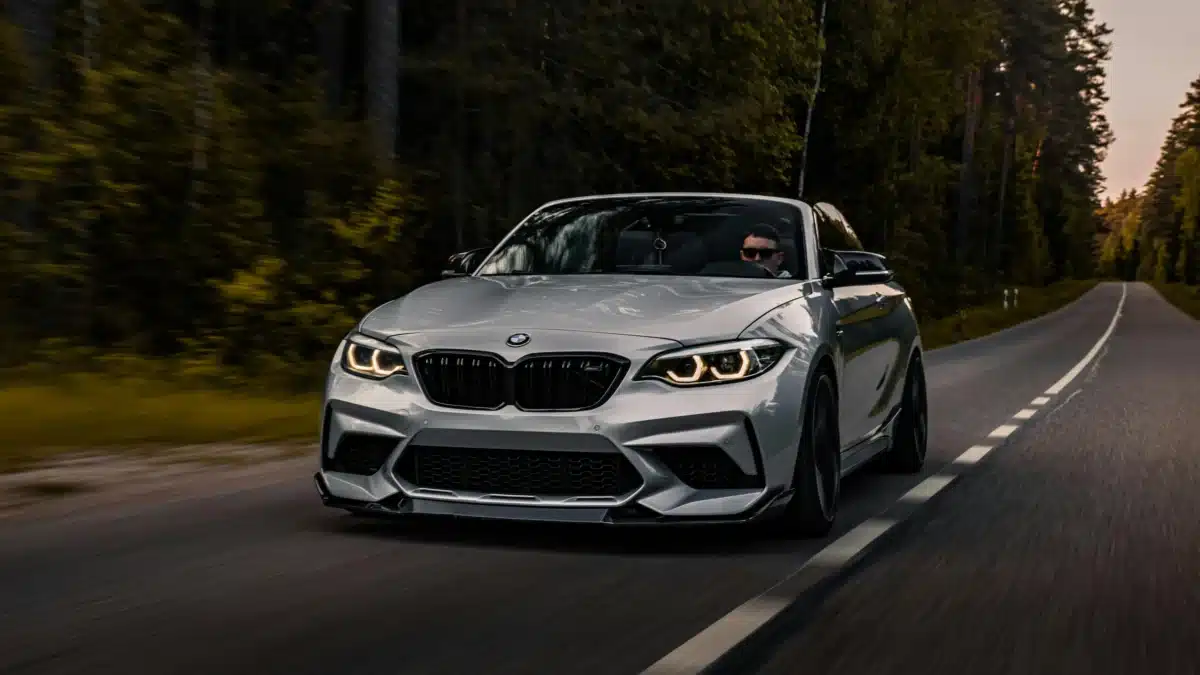 A silver BMW with tinted windows is driving down a road in the forest.