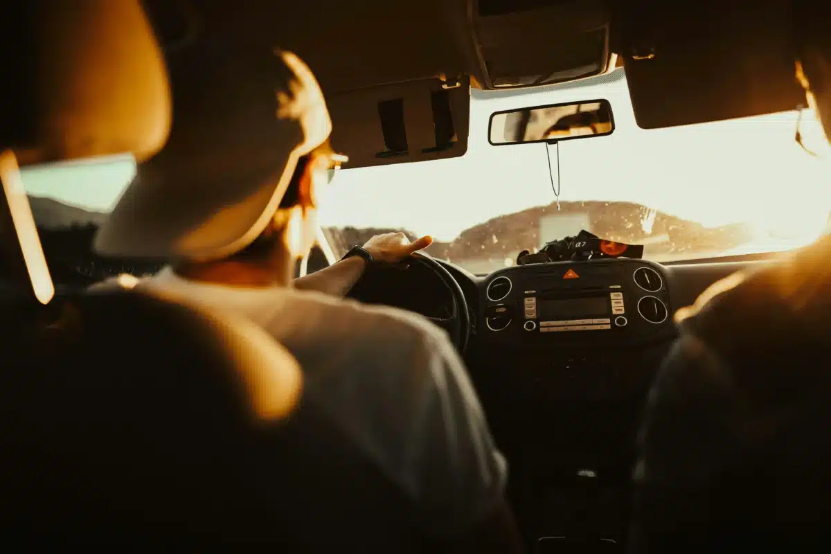 An over the shoulder view of a young man driving a car wearing a backwards baseball cap. He's driving towards he sun on a freeway toward Carzwerk for car detailing near Manteca CA.