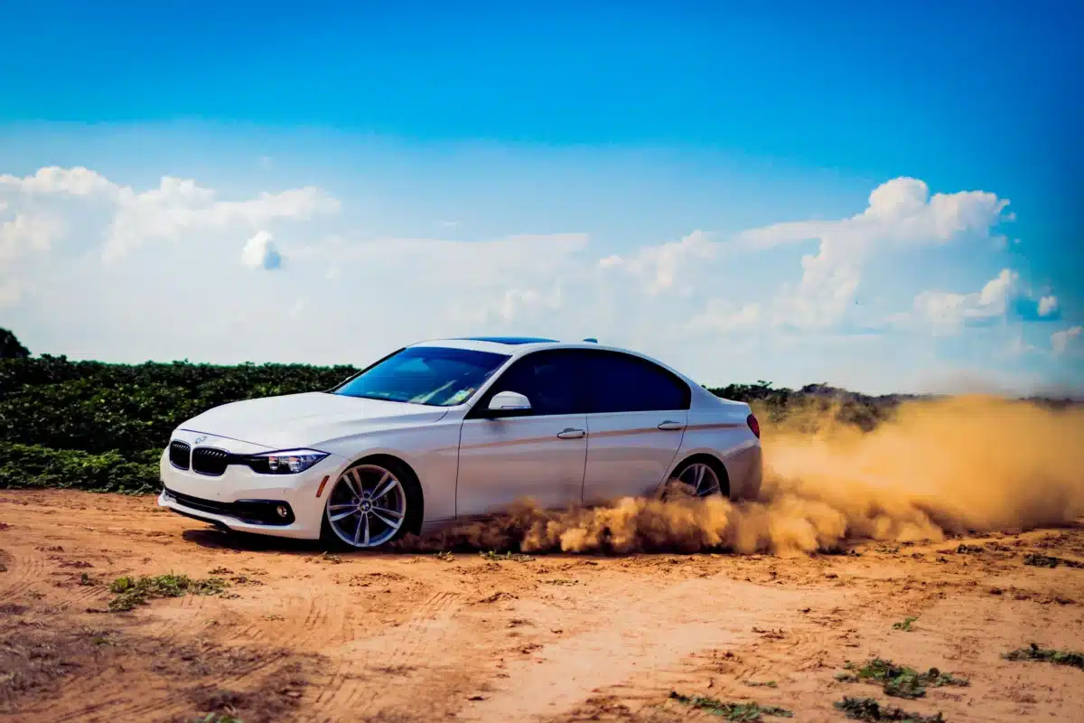 A BMW with tinted windows in Santa Clara driving through a dirt road on a sunny day.