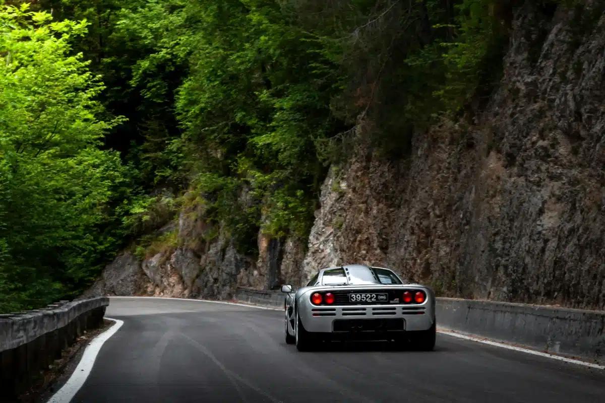 A grey Porsche is being driven on a tree-lined street. 