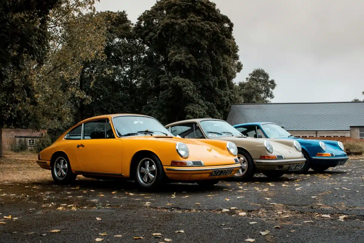 Three vintage Porsche cars, from left to right, are Orange, Tan, and Blue. 